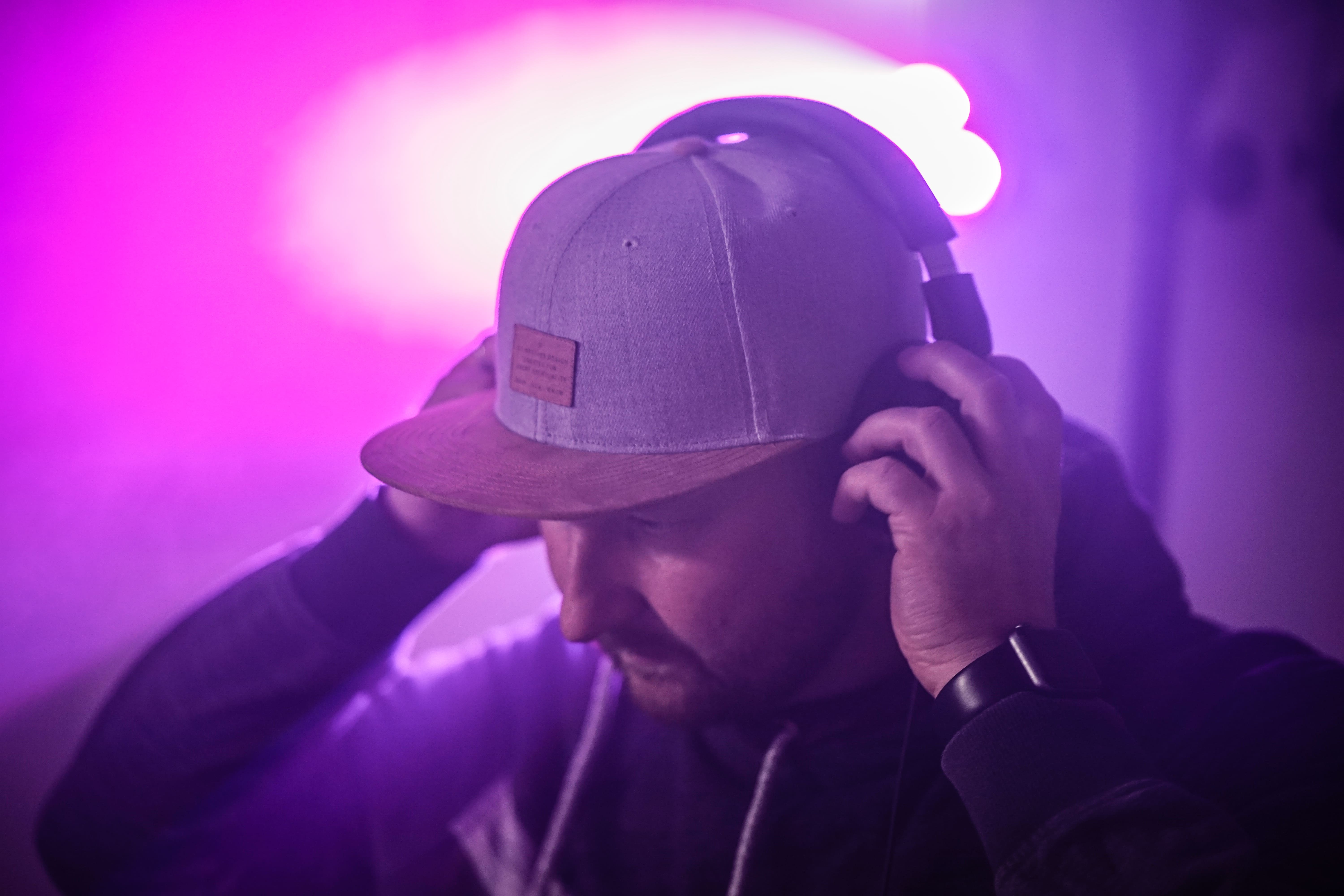 DJ Tony Lötzke mit Kopfhörern und Cap unter violetter Bühnenbeleuchtung