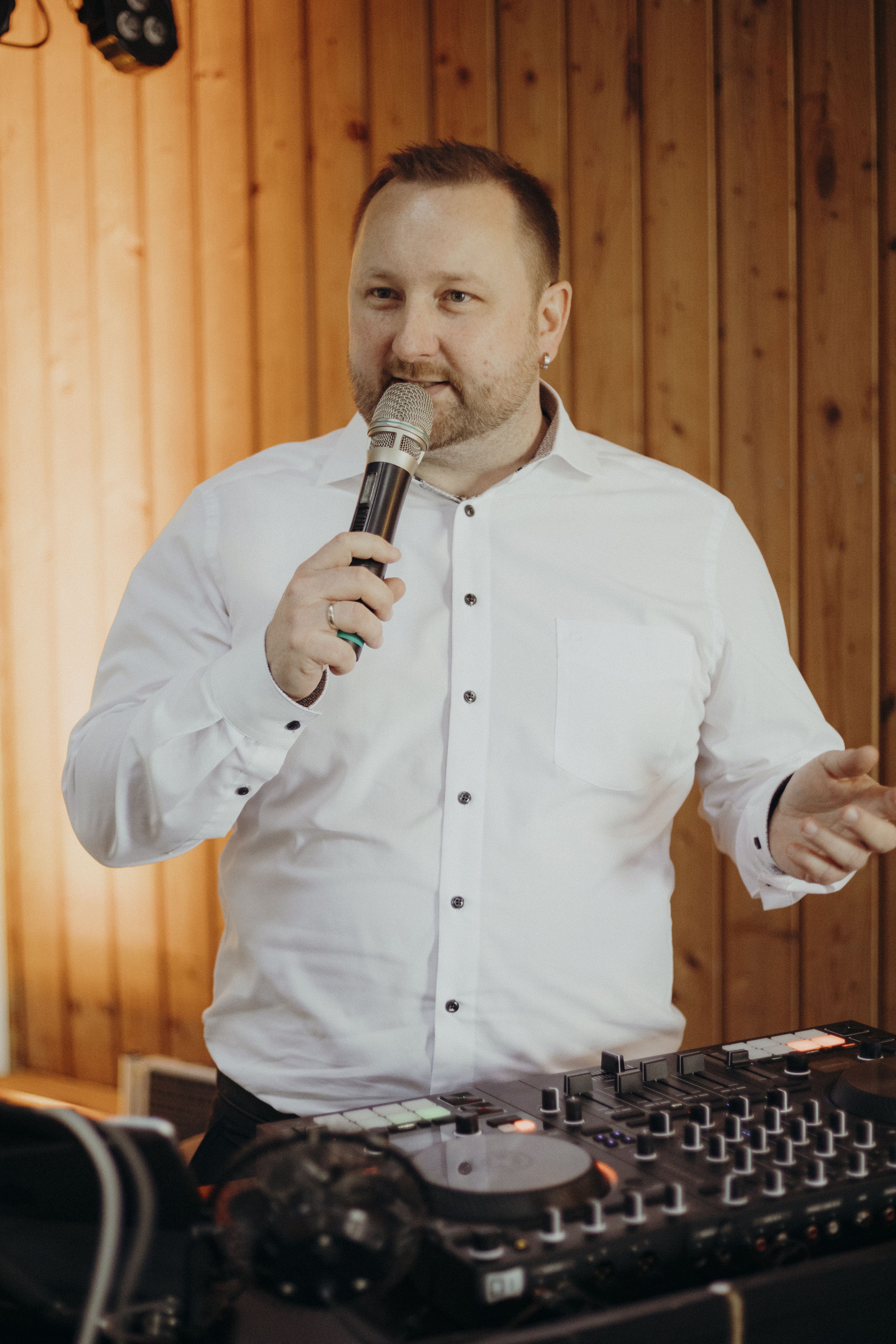 Hochzeits-DJ Tony Lötzke moderiert mit Mikrofon am DJ-Pult bei einer Hochzeitsfeier