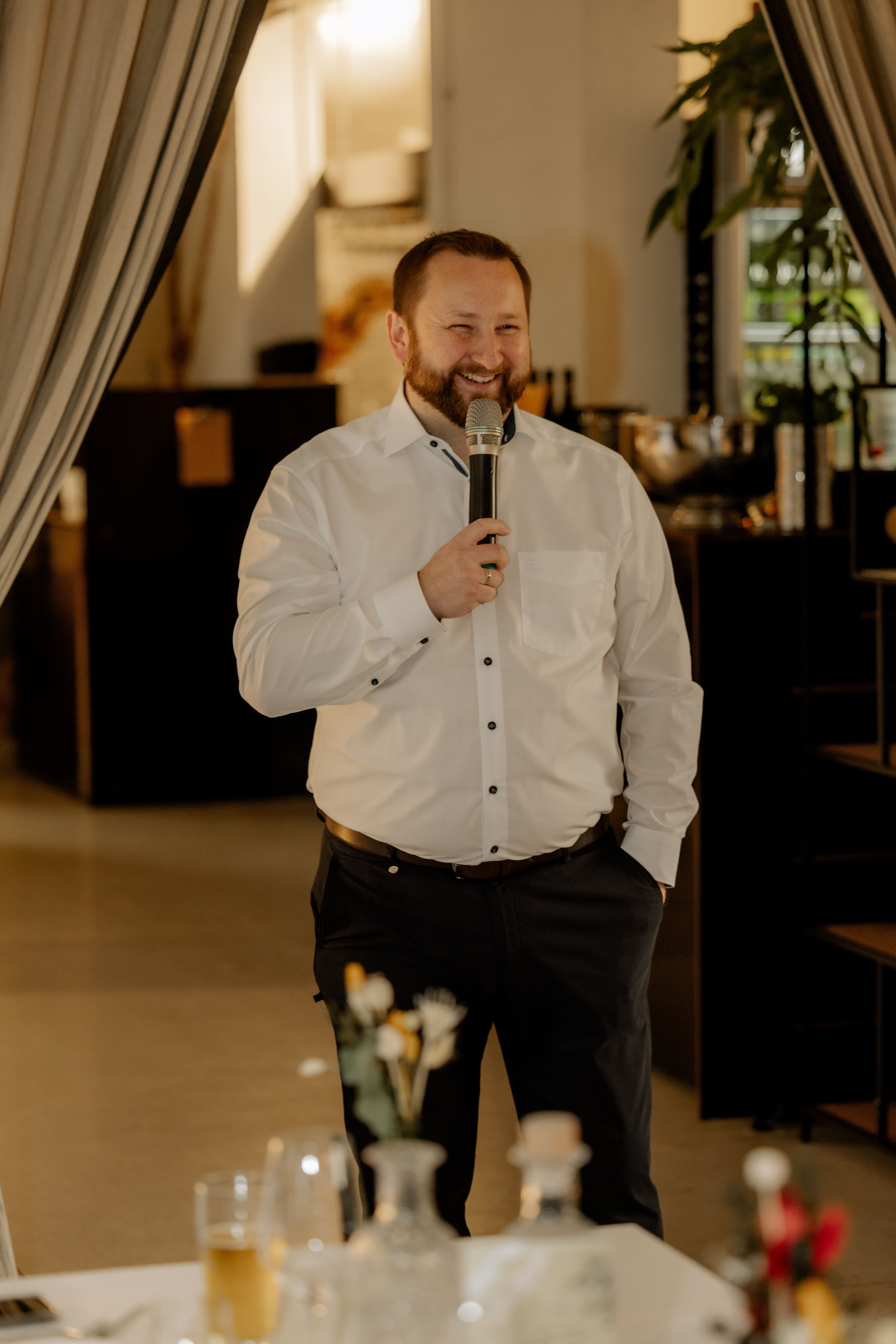 Hochzeits-DJ Tony Lötzke lächelt herzlich mit Mikrofon in einem eleganten Hochzeitssaal
